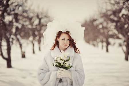 Braut im Freien mit Brautstrauß, Schleier und Mantel im Winter