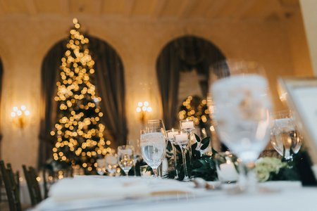 festliche Tischdekoration einer Winterhochzeit mit leuchtendem Weihnachtsbaum im Hintergrund